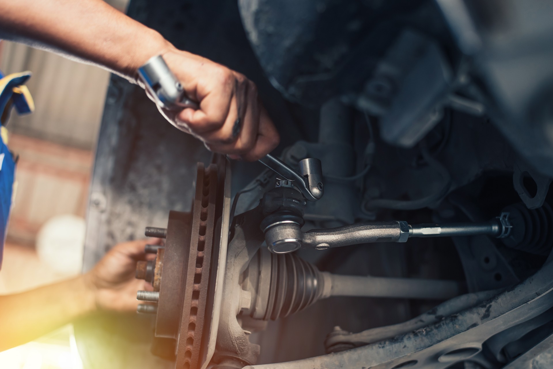 At a repair shop, a car mechanic tightens the suspension of an elevated vehicle with a spanner.